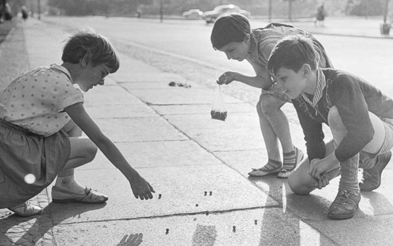 Drei Kinder im Grundschulalter spielen auf einem Bürgersteig mit Murmeln, (Ausschnitt) 1964. SW-Foto © Kurt Schwarz. (CC BY-NC-SA) - kinderspiel